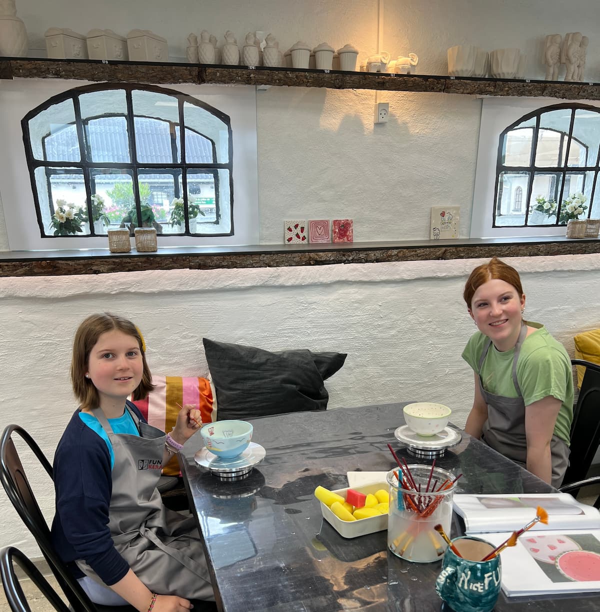 To piger sidder og smiler ved bord og laver keramik hos Funart Keramik - Oplevelser for børn i Nordjylland.
